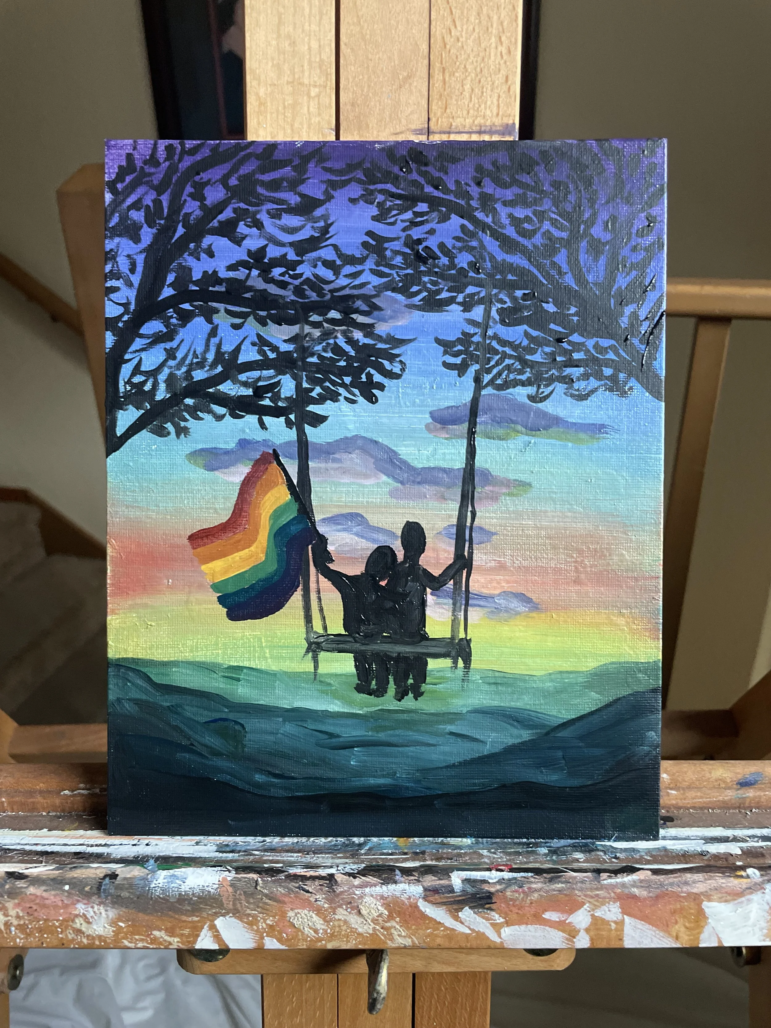Painting of two people on a swing hanging from a large tree, holding a rainbow pride flag, with a colorful sunset sky and mountains in the background.