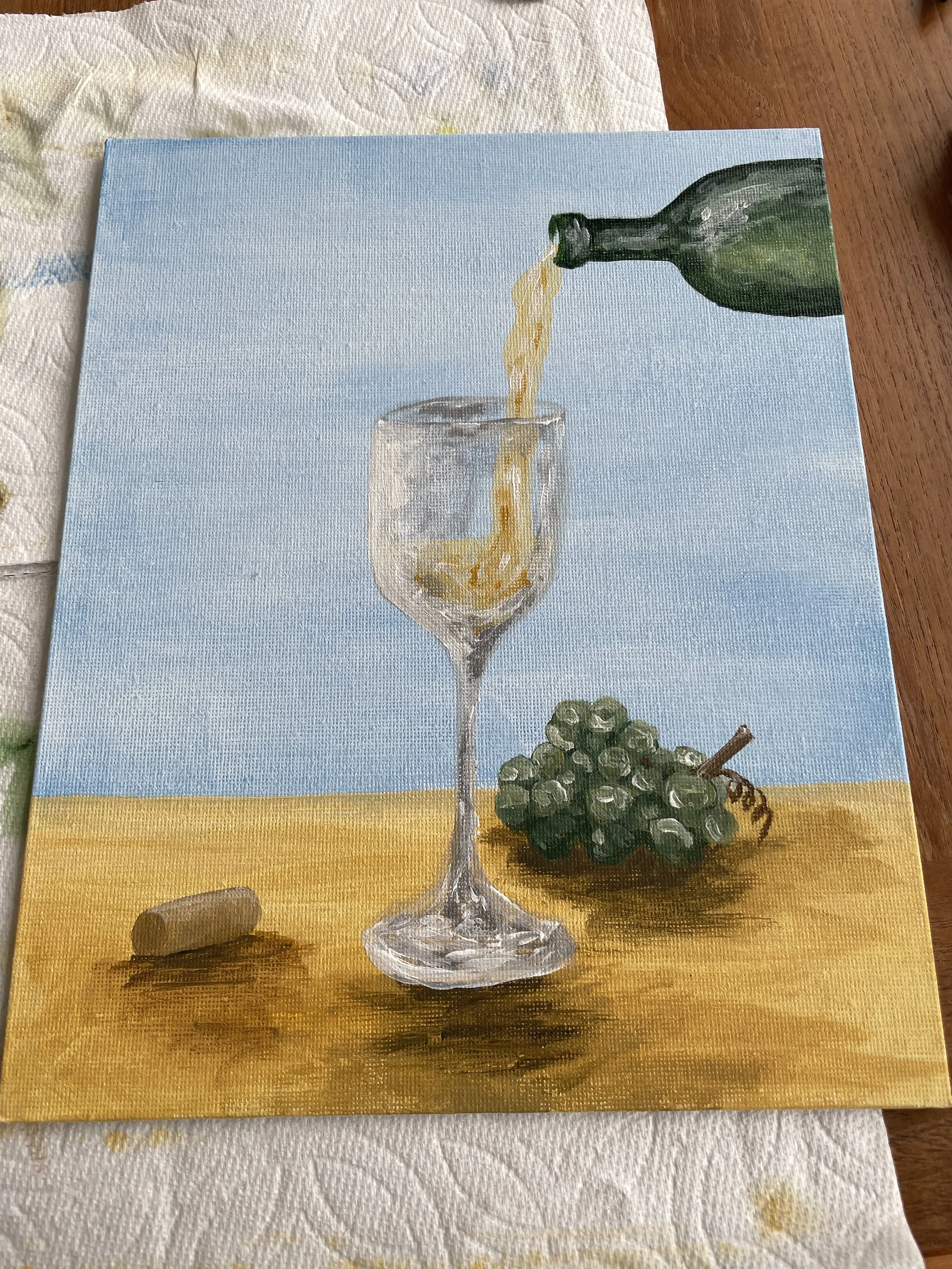 Painting of a drop of champagne pouring into a glass, with a bunch of green grapes and a cork on a wooden surface against a blue sky background.