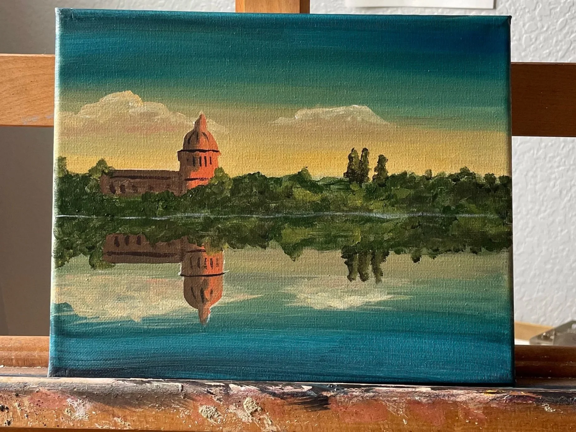 Painting of a building with a dome, reflecting in a calm body of water, during sunset or sunrise with a mostly clear sky.