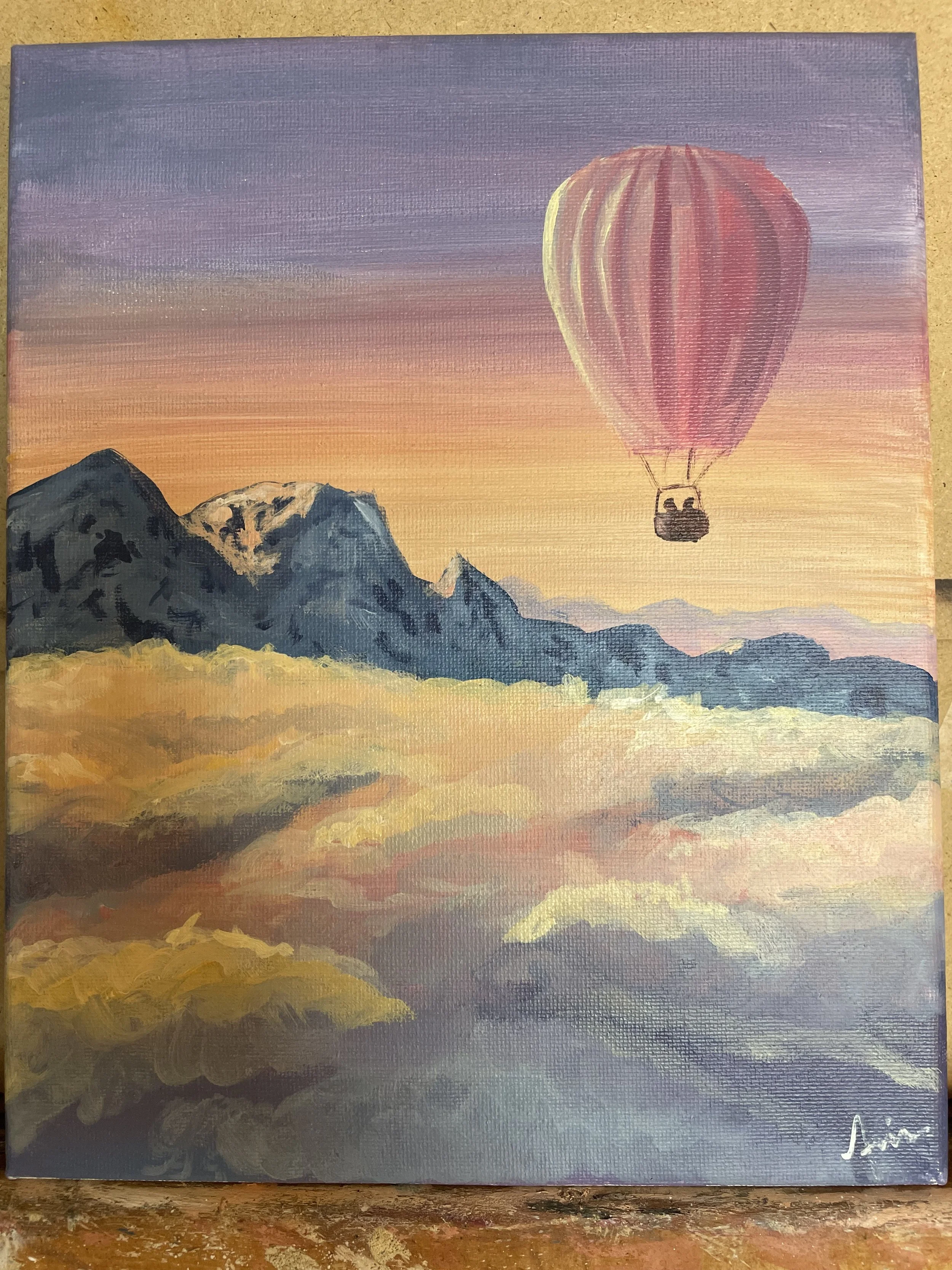 A UFO-shaped hot air balloon flying over mountains at sunset with clouds below.