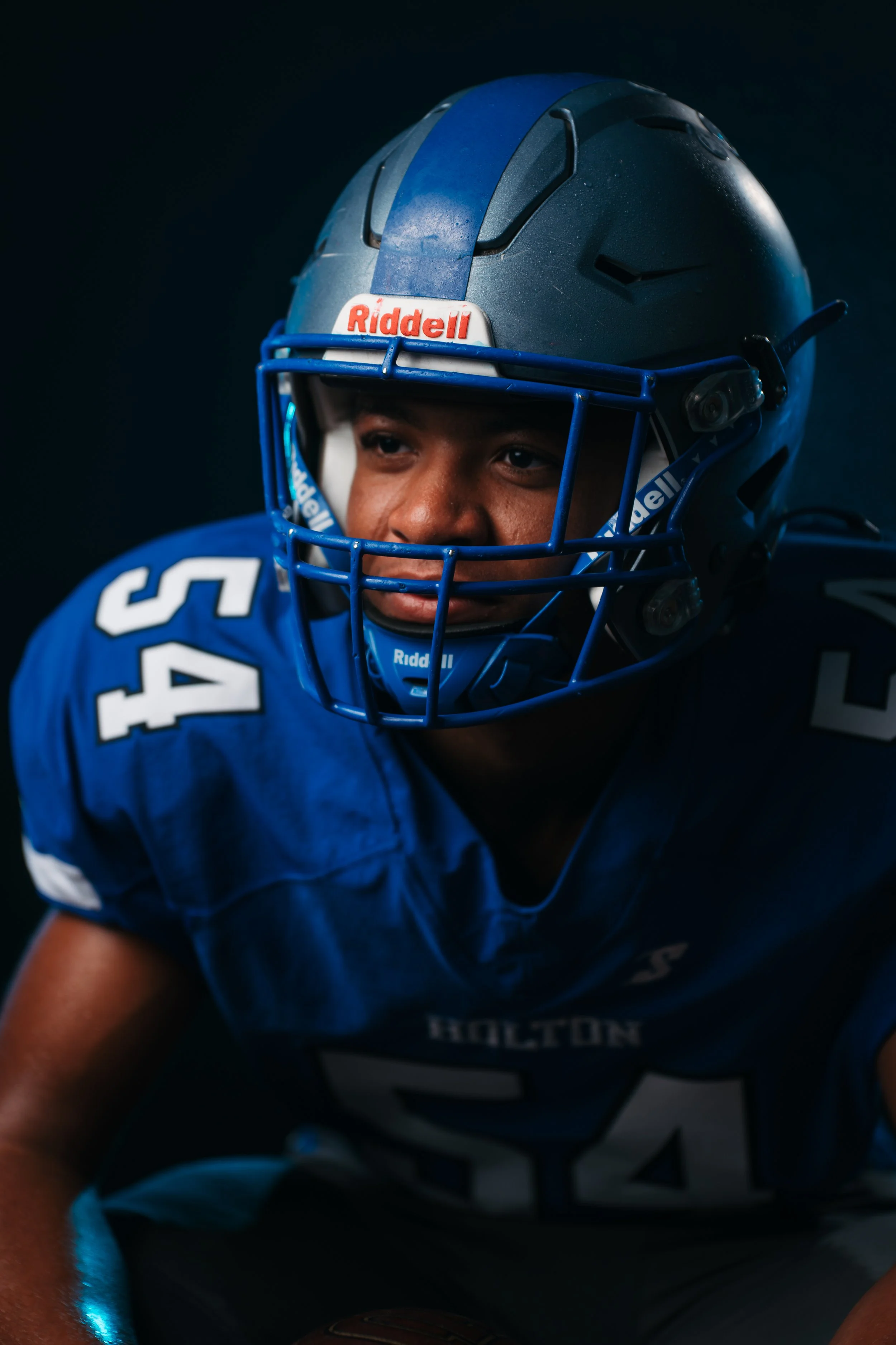 A football player in a blue helmet and jersey crouches for a game or photo shoot.