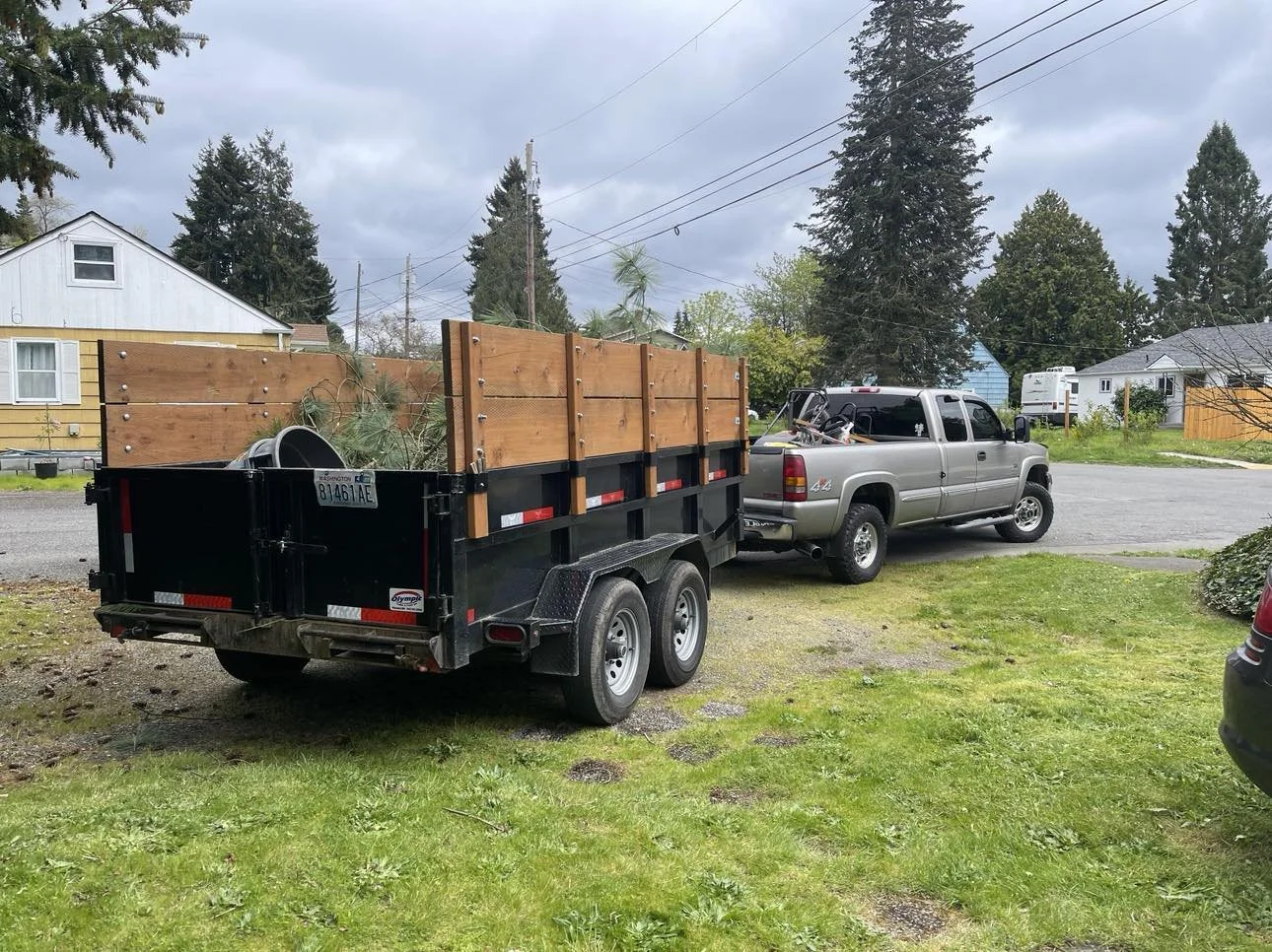 A pickup truck with a trailer attached is parked on a lawn, with houses and trees in the background under an overcast sky.