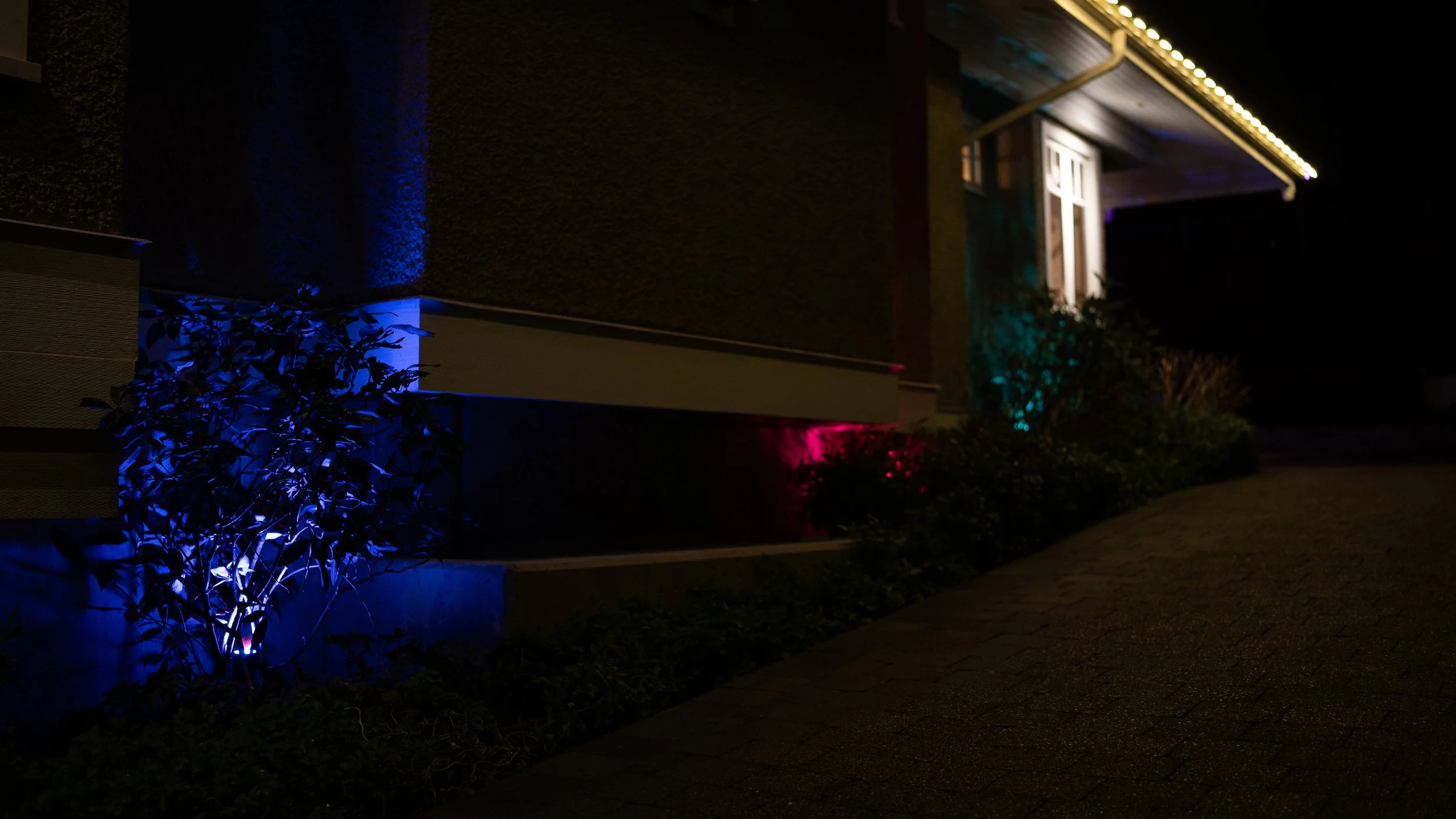 Close-up of a modern house's window with red and black exterior siding, reflecting trees and a cloudy sky.