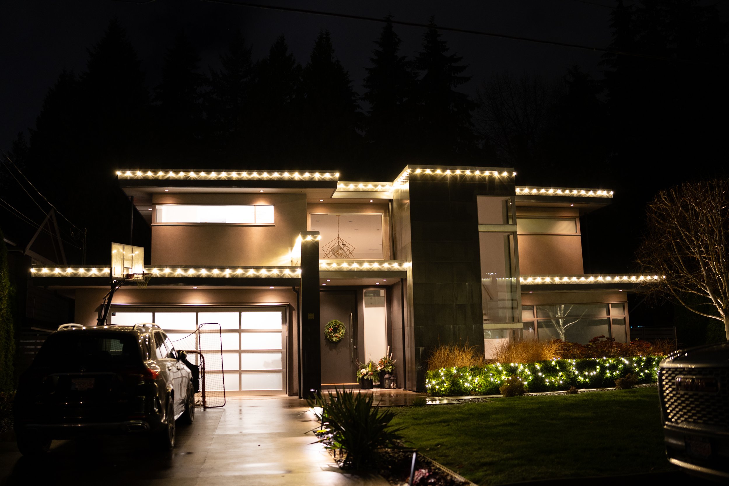 View of house roofs with skylights and vents, some wet from rain, with trees and neighboring houses in the background.