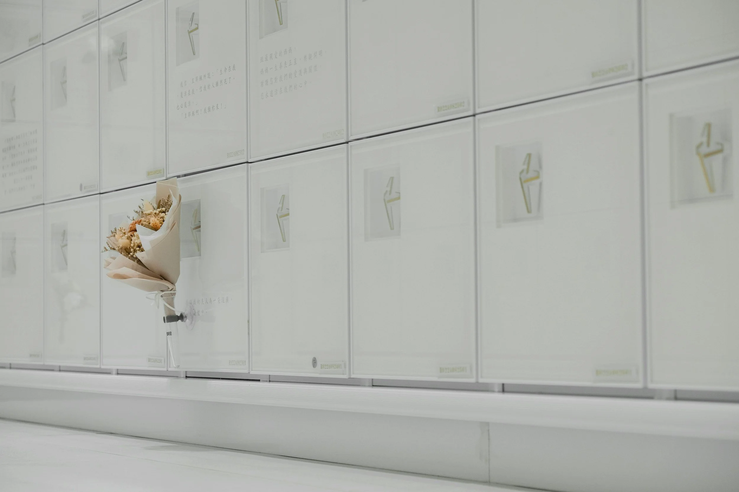 A bouquet of flowers taped to a white wall of mailboxes in an indoor setting.