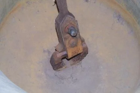 Close-up of a rusty mechanical part submerged in a yellowish liquid.