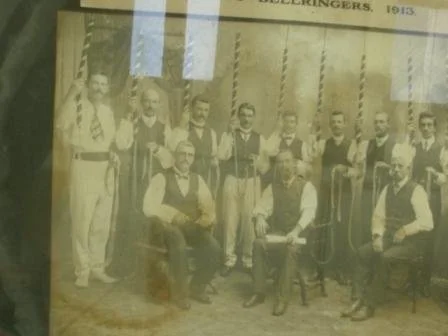 Historical black and white photograph of a group of men standing and sitting in front of a decorated backdrop, dated 1913.