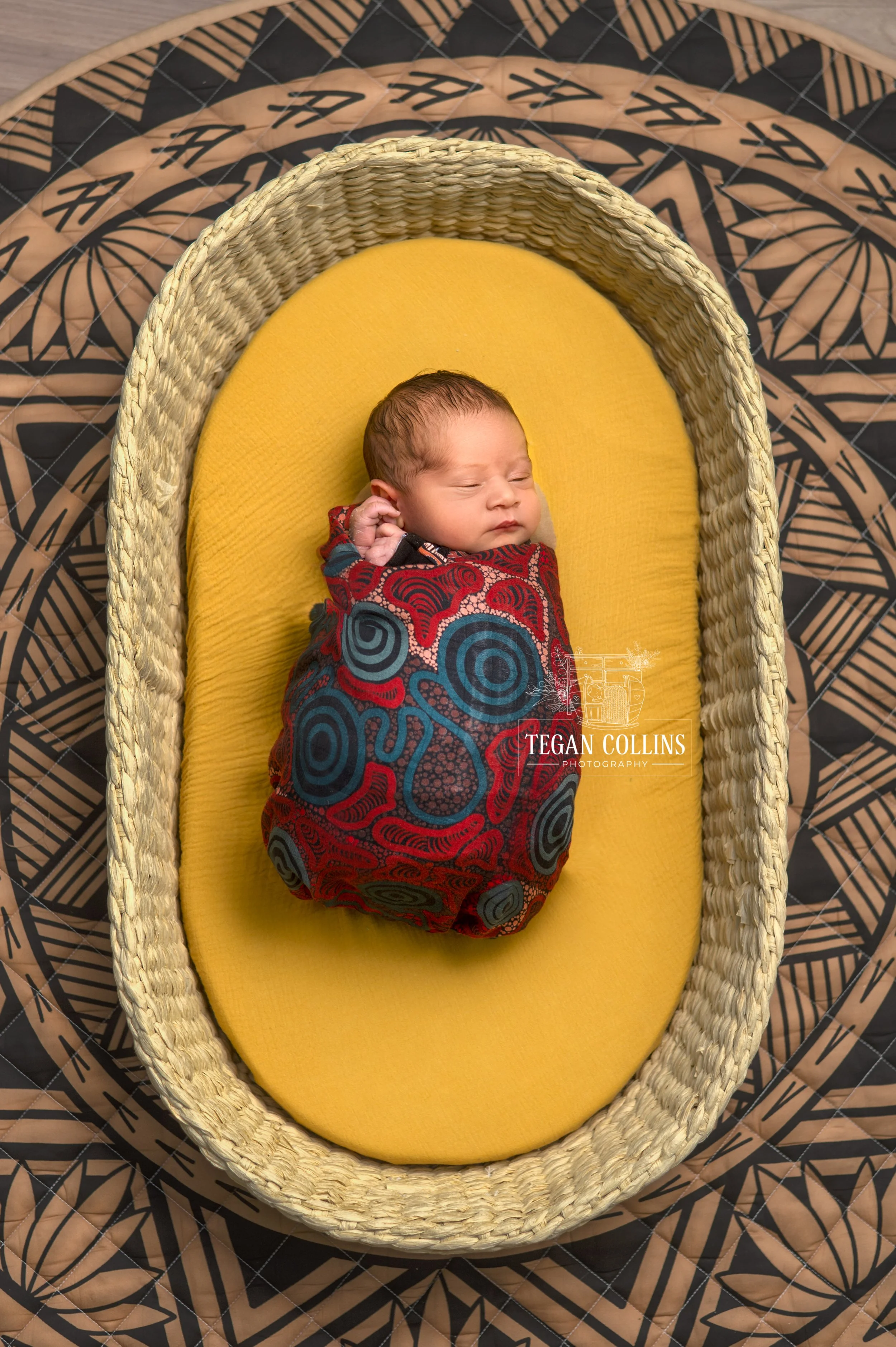 A newborn baby asleep in his basket on a fijian rug.