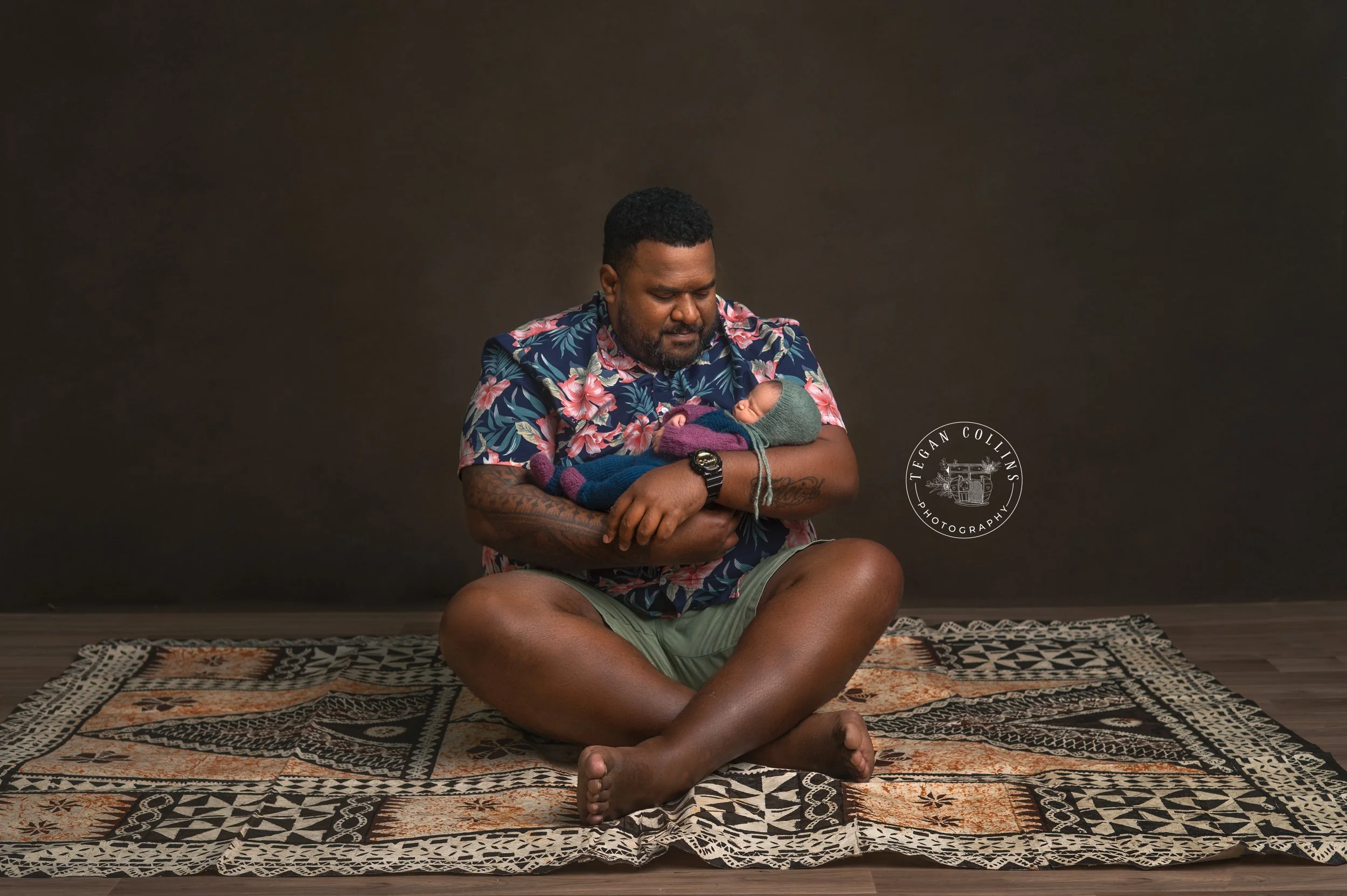 A dad holds his brand new baby girl on his Fijian rug. 
