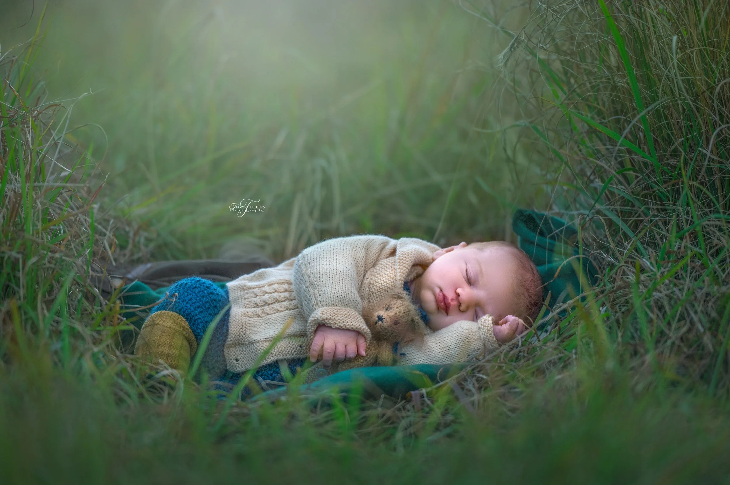 a newborn baby lays down amongst the grass and naps while holding a teddybear