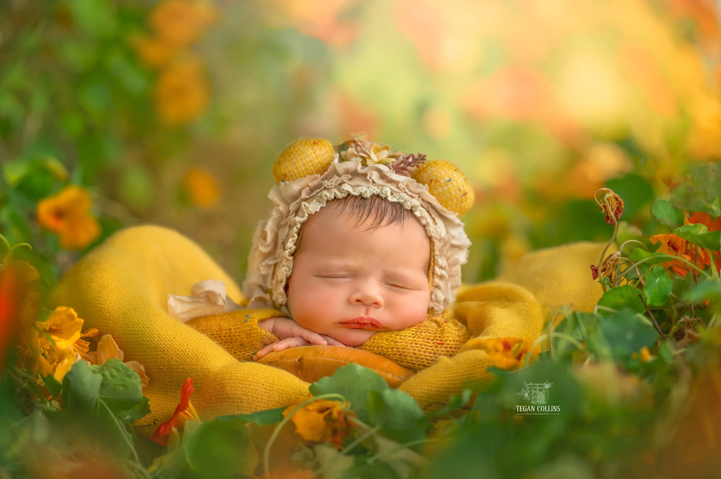 A newborn baby girl with her chin on her hands sleeps soundly among the yellow flowers.