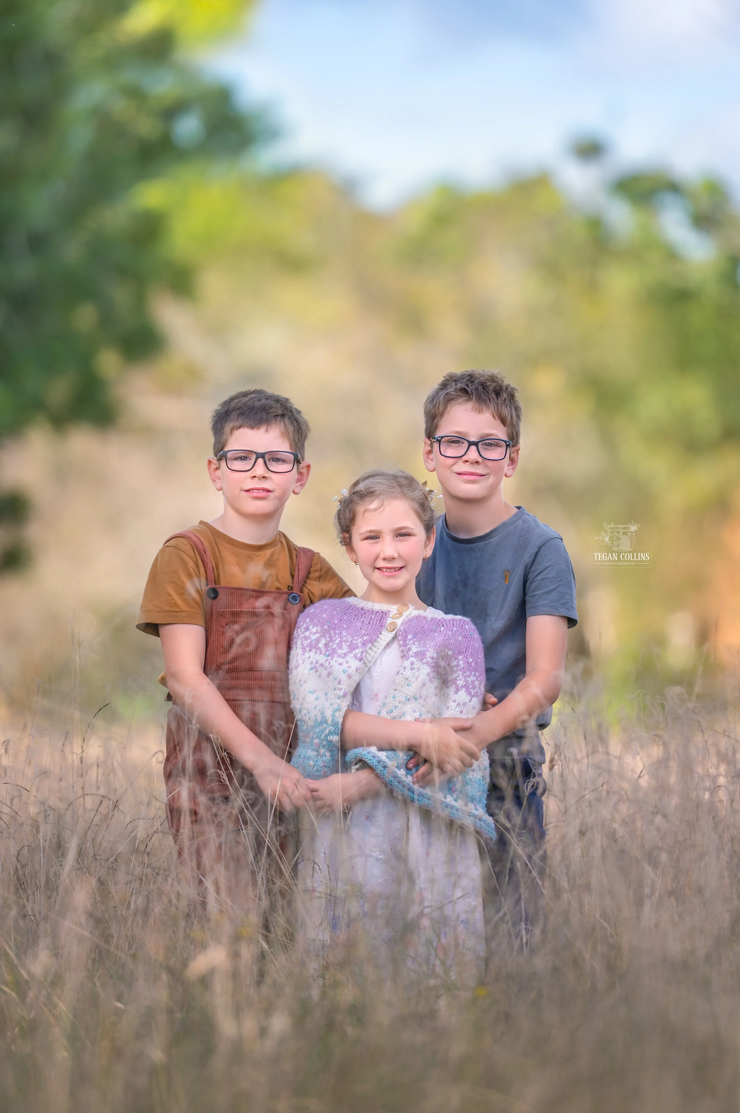 Two brothers stand behind their younger sister in a field full of winter grass'