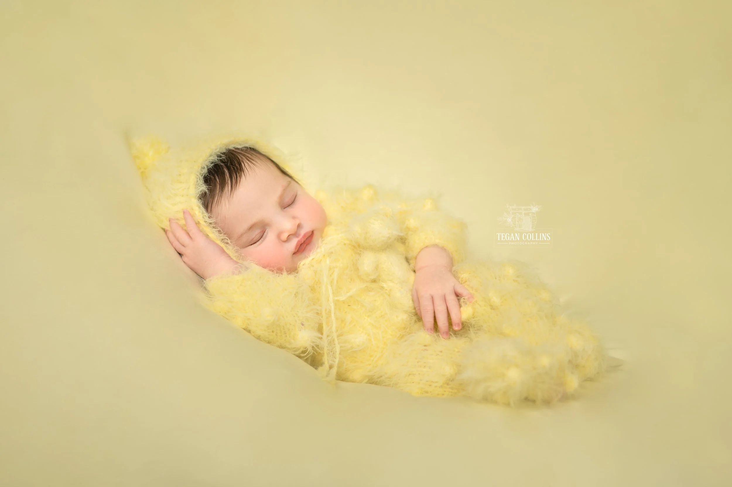 a newborn baby wearing a yellow fuzzy knitted suit on a blurred yellow background