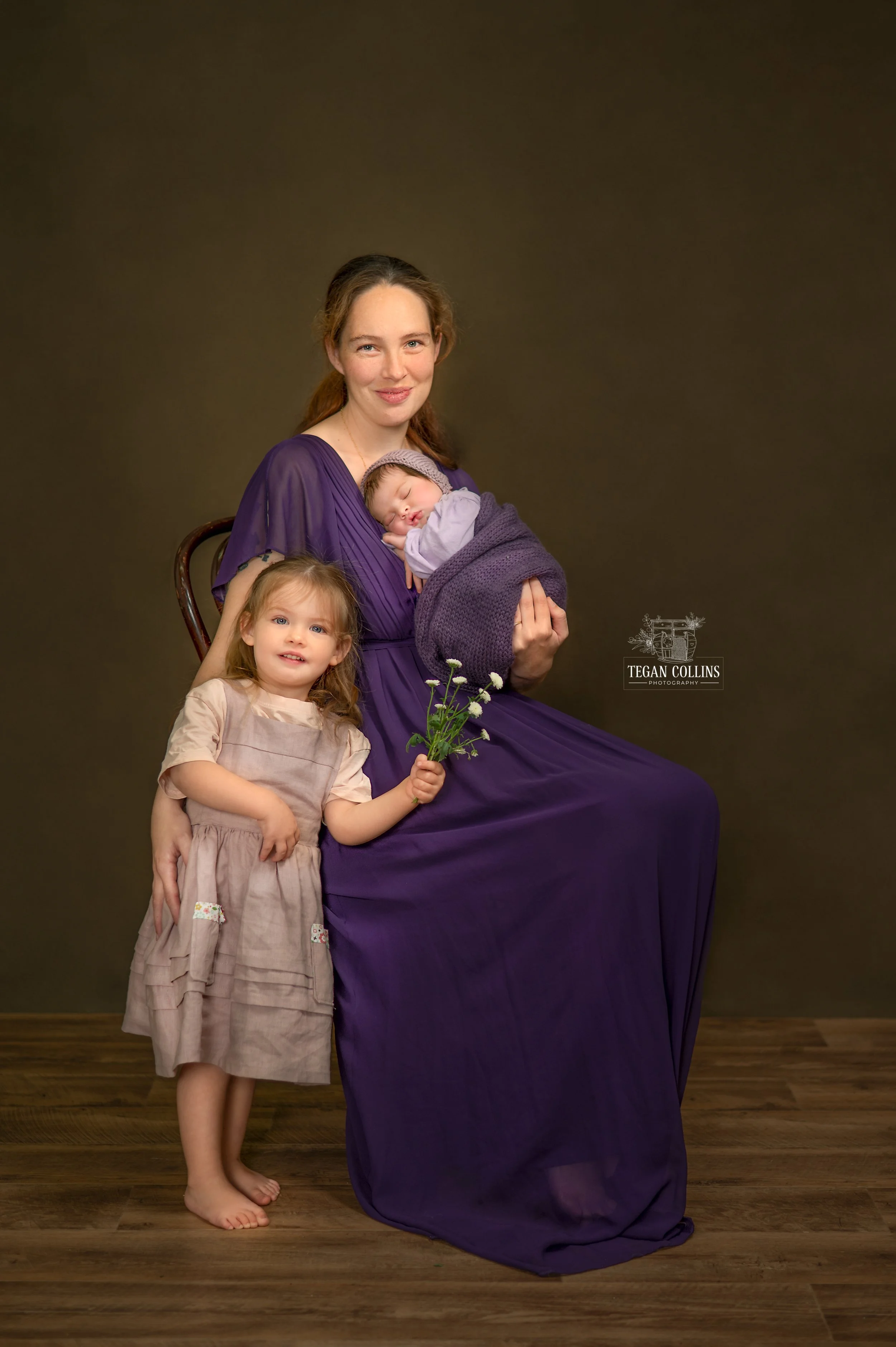 Mum holds her newborn baby while also snuggling her eldest daugher