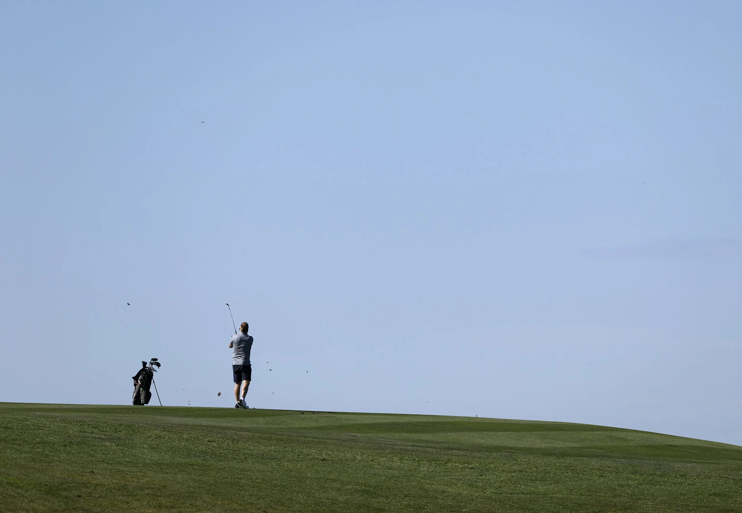 A golfer hits the ball on hole 6 at Pebble Beach Golf Links, with a blue sky in the background