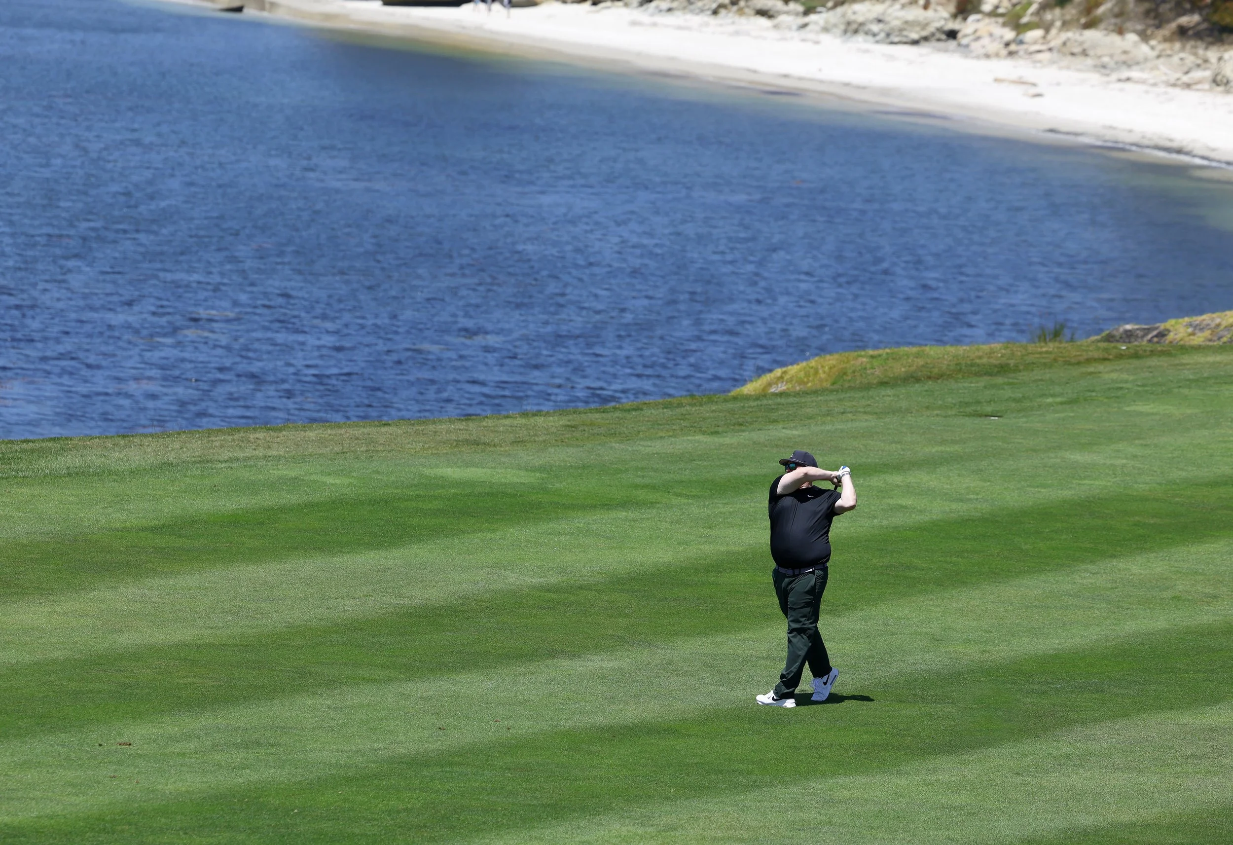 A golfer hits the ball from the fairway on hole 6 at Pebble Beach Golf Links with a blue ocean behind him