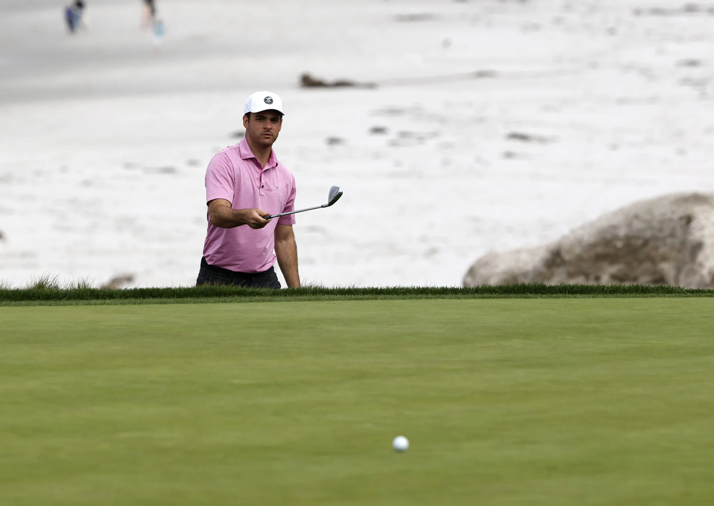 A golfer in a pink shirt watches his ball roll on the green at Pebble Beach Golf Links