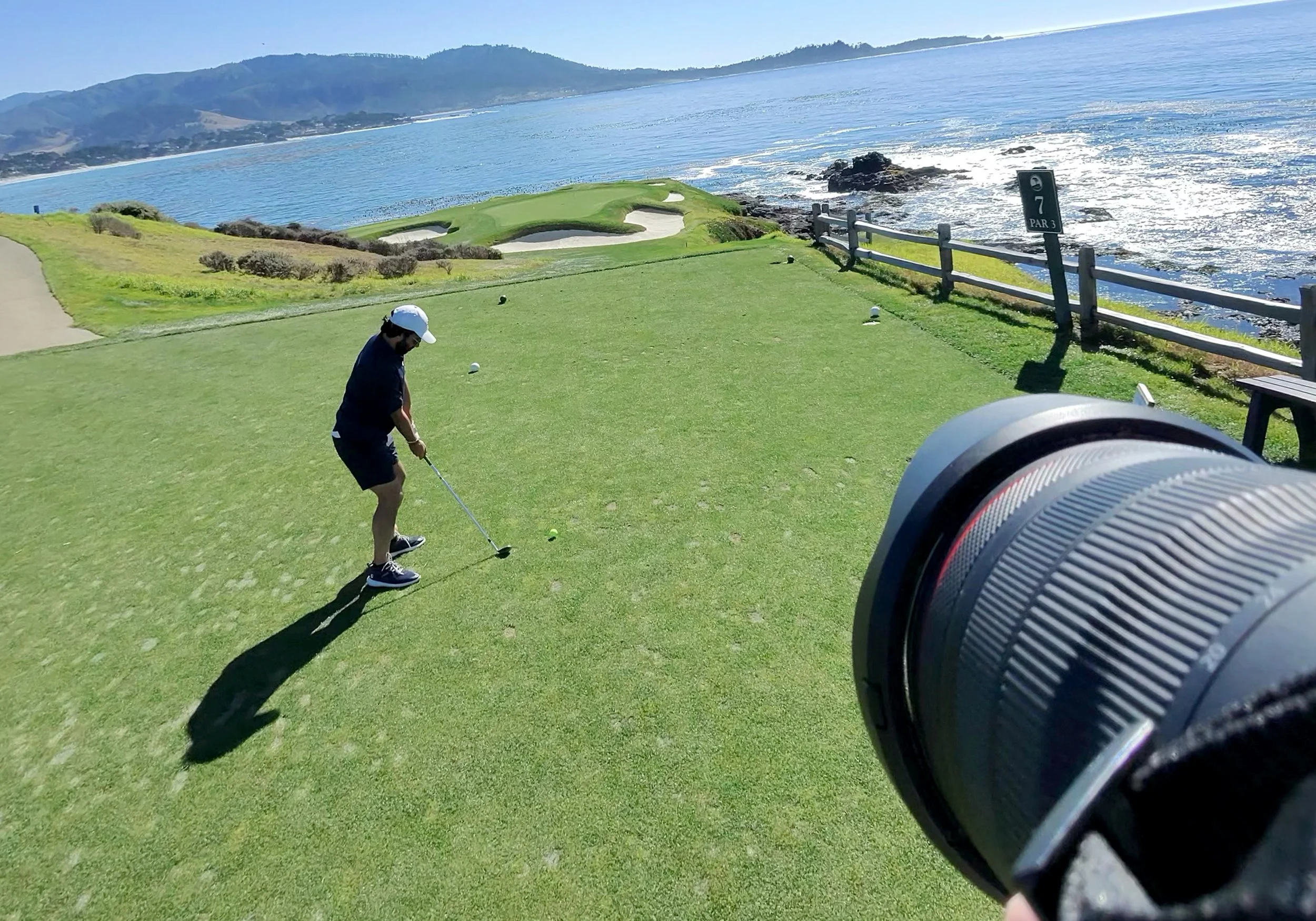 A photographer takes a photos well a golfer tees off on the famous 7th hole at Pebble Beach Golf Links