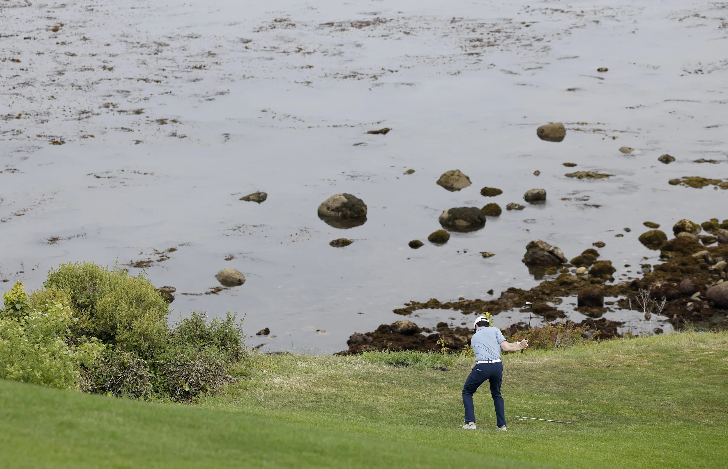 A golfer in a blue shirt hits the ball from the fairway on the 6th hole at Pebble Beach Golf Links
