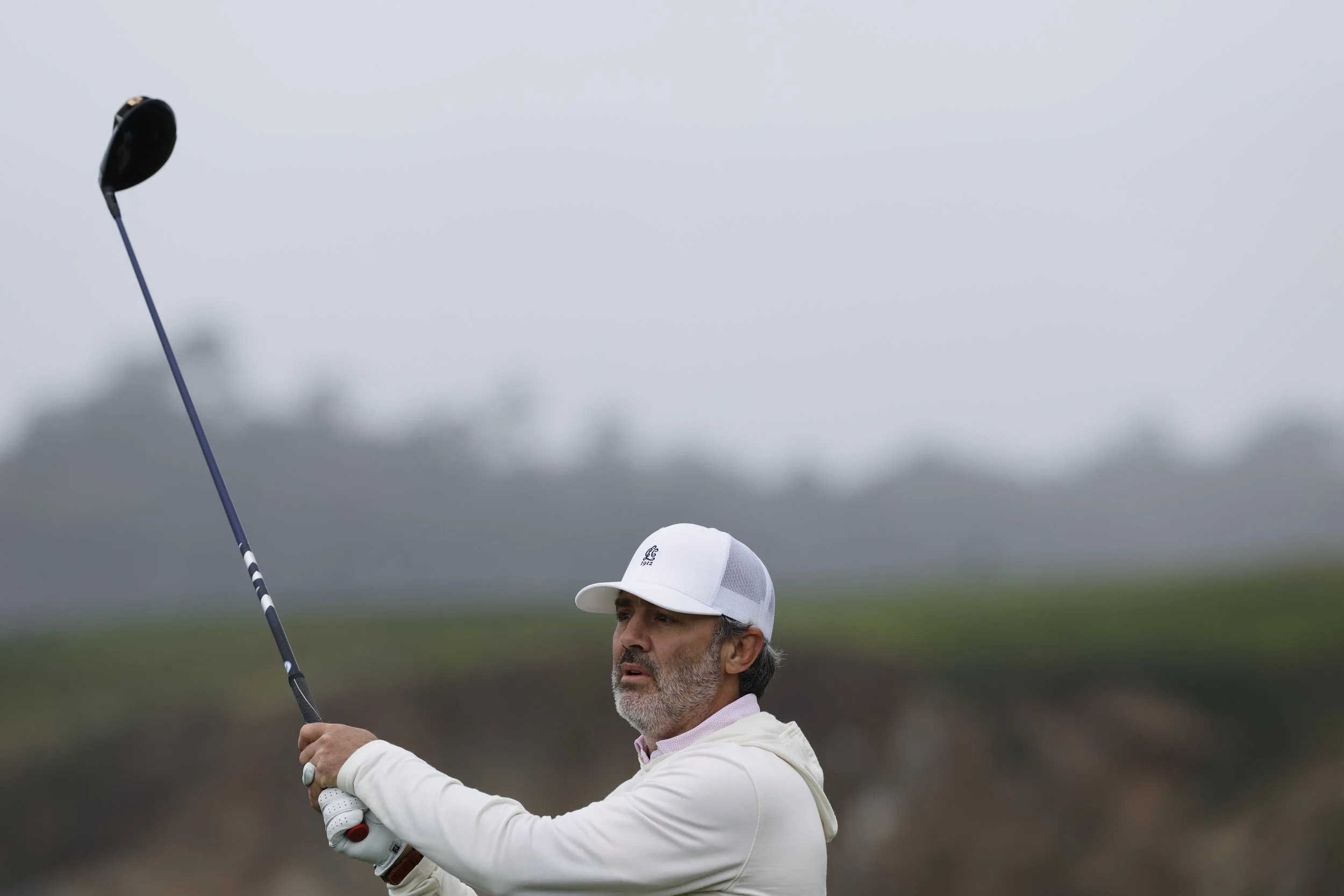 A golfer in a white hat hits the ball at Pebble Beach Golf Links