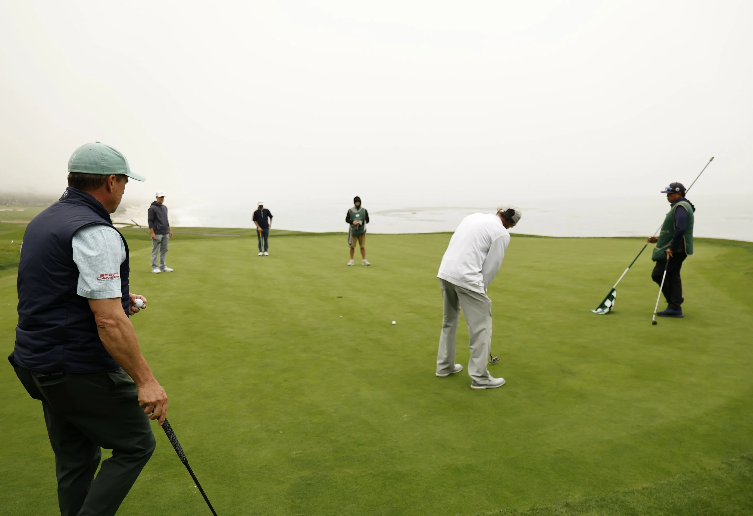 A golfer in a white shirt putts the ball on the 8th hole at Pebble Beach Golf Links