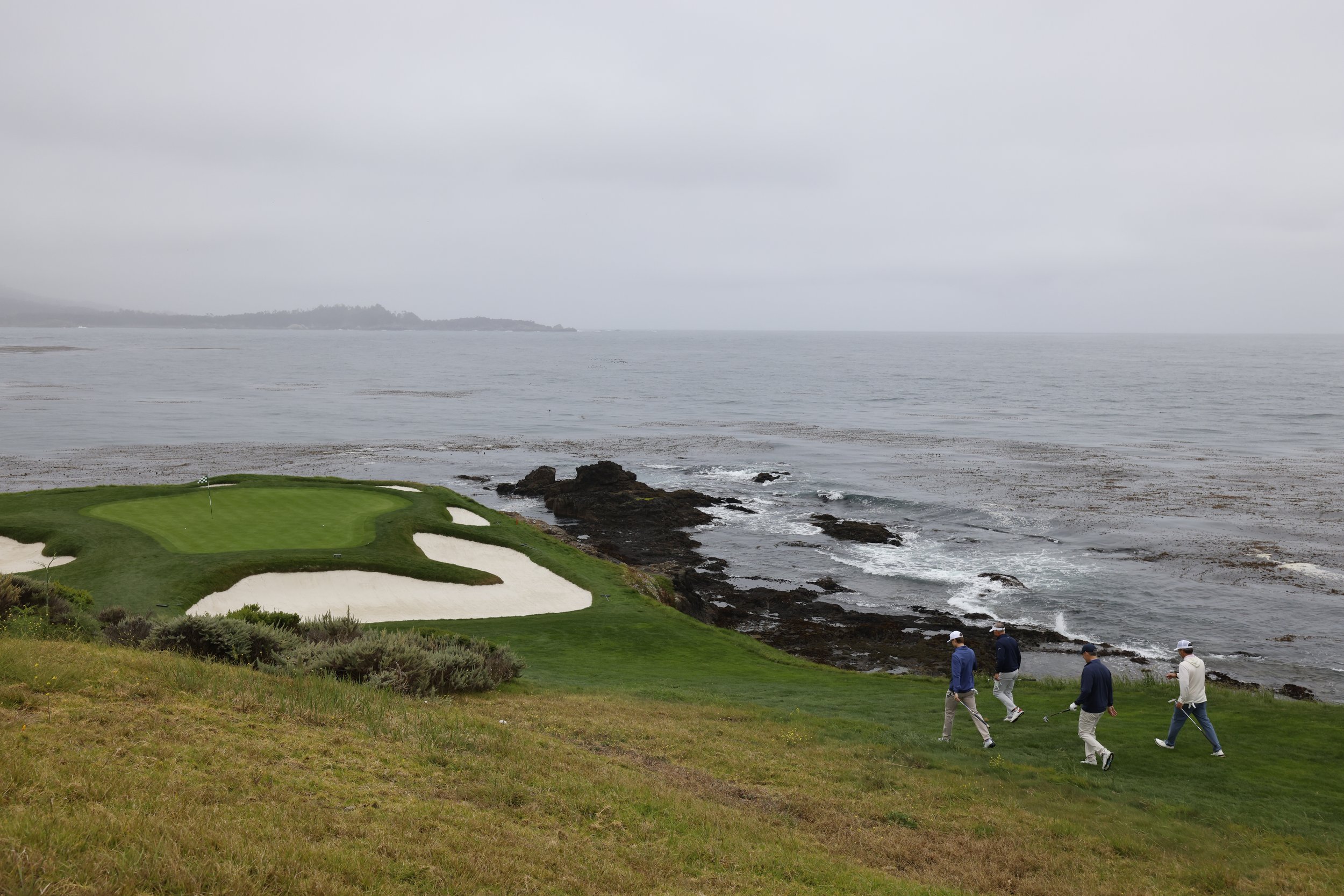 A group of golfers walk the iconic 7th hole at Pebble Beach Golf Links