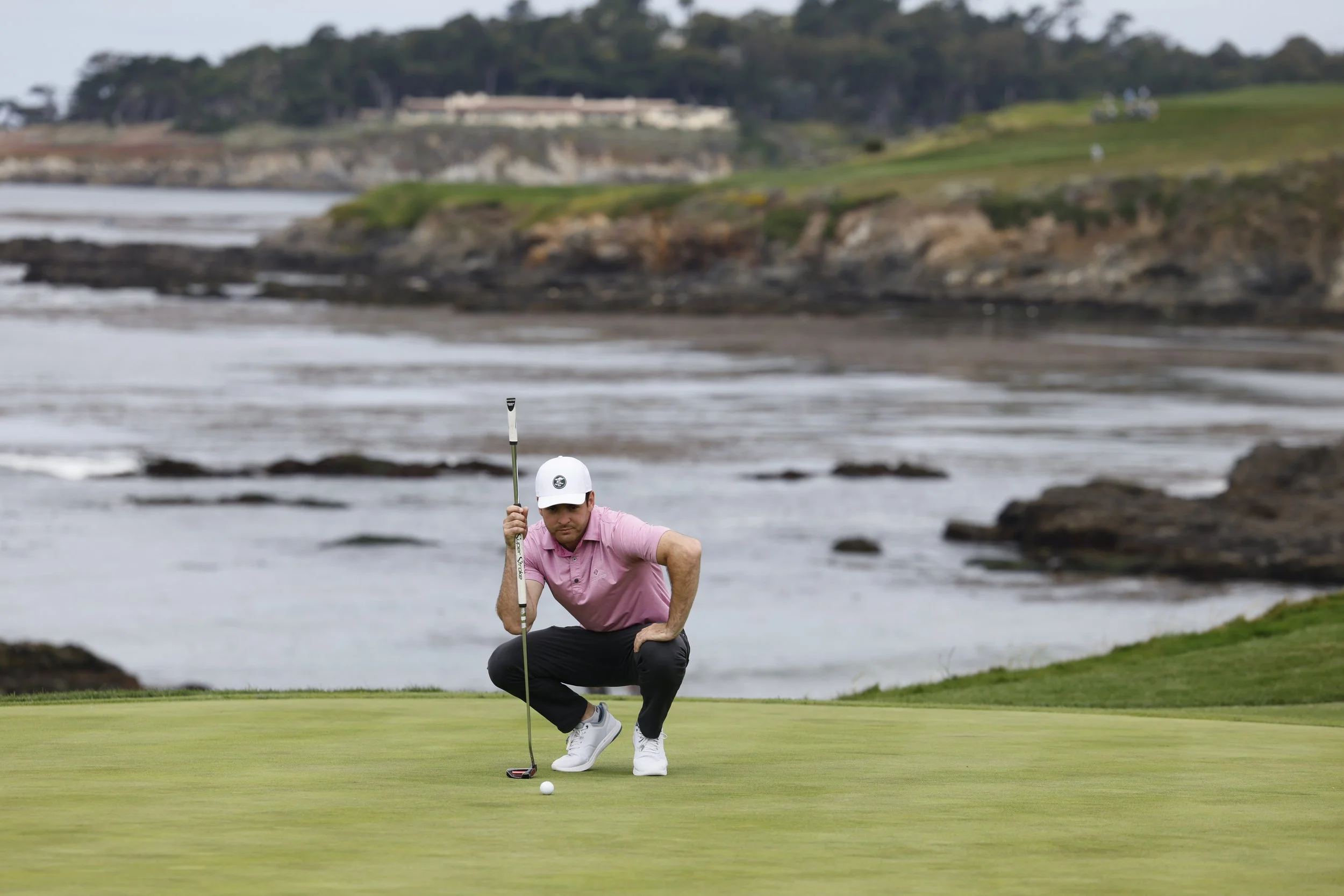 A golfer in a pink shirts lines up his putt at Pebble Beach golf Links.