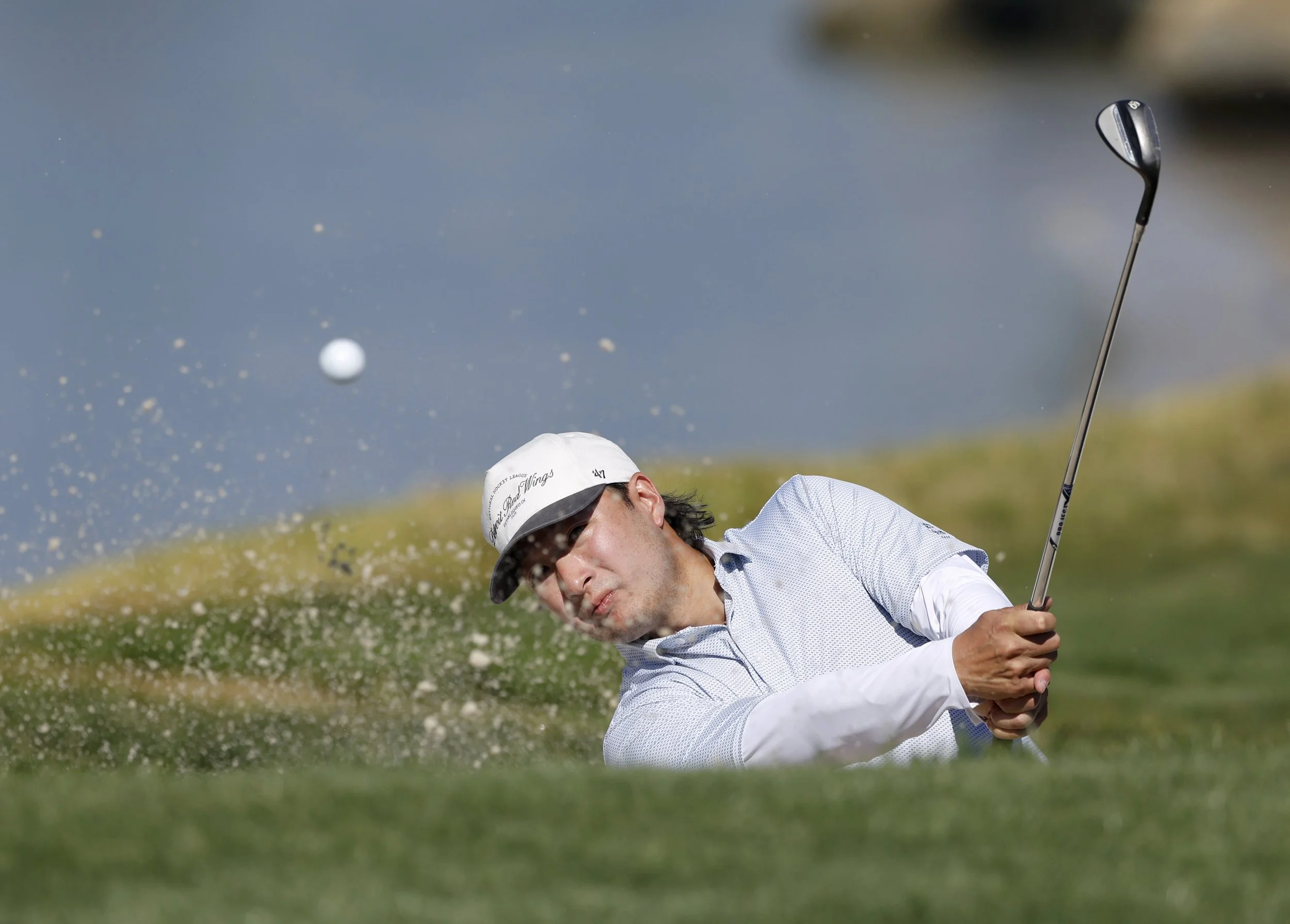 A golfer in a white shirt hits the ball out of a sand trap at Pebble Beach Golf Links