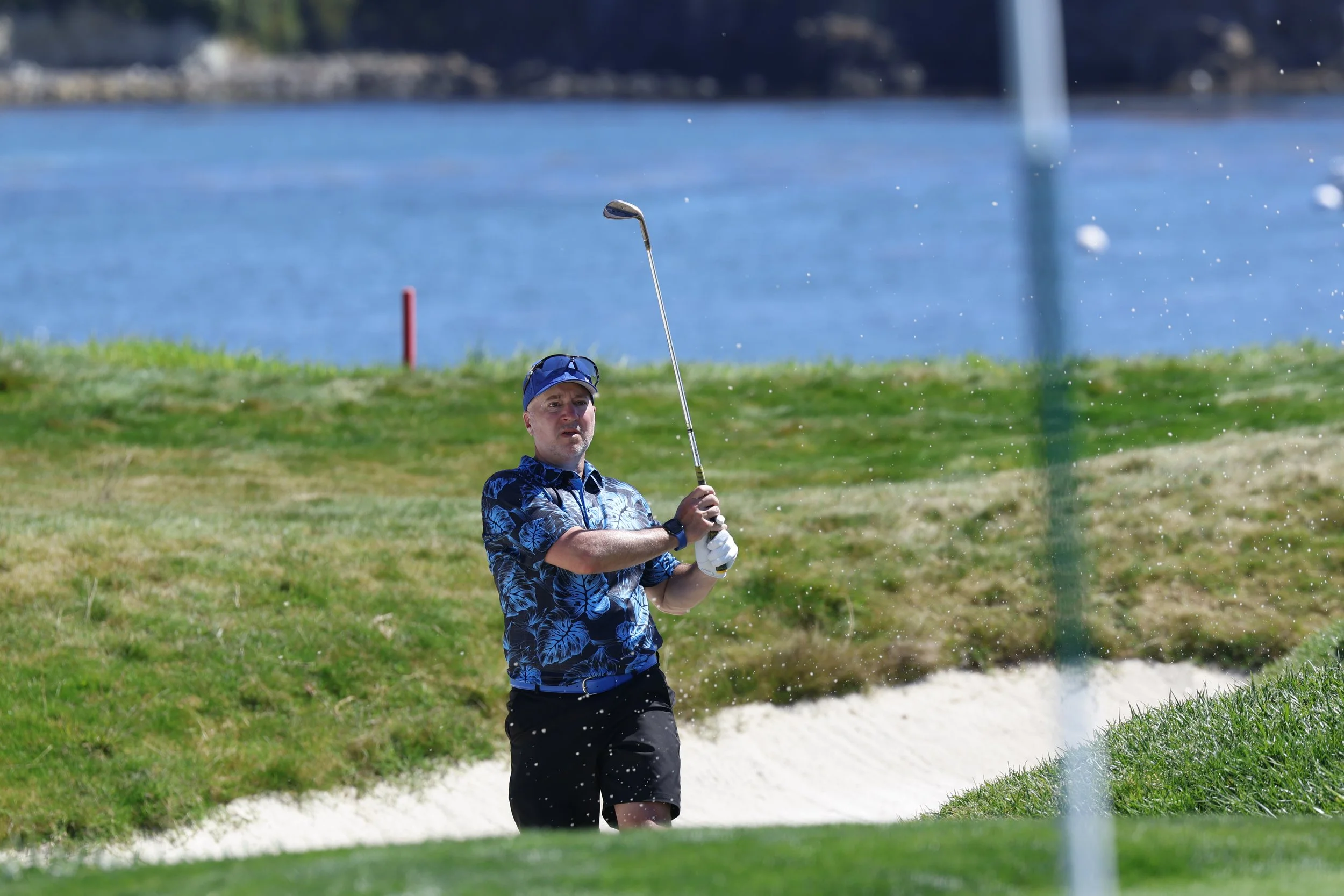 A golfer in a blue shirt hits the ball out of a sand trap on the 6th hole at Pebble Beach Golf Links