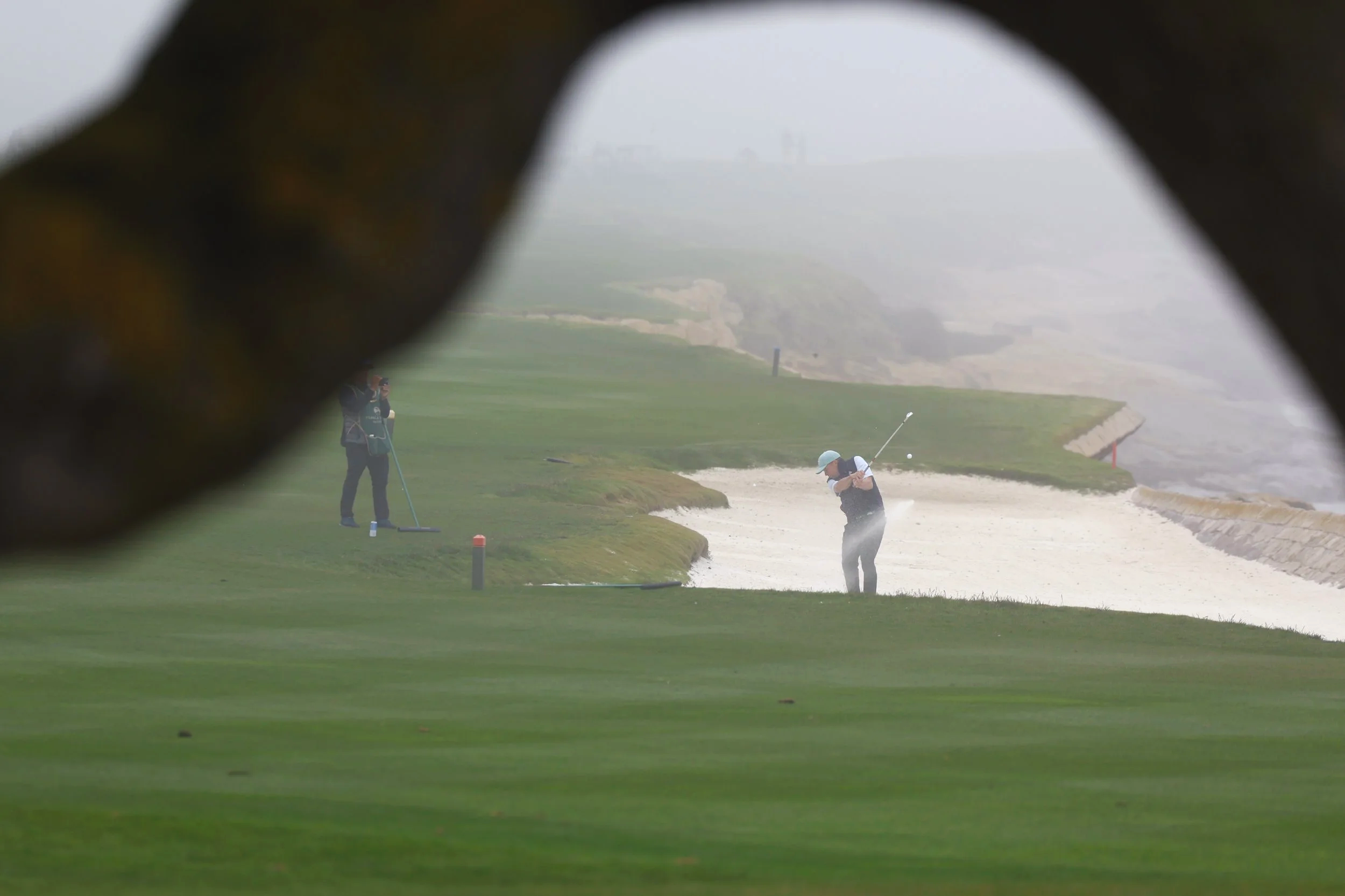 A golfer hits the ball from a sand trap on hole 18 at PEbble Beach Golf Links on a foggy day