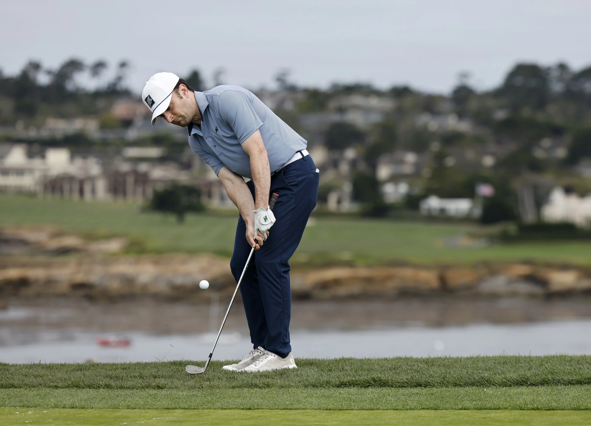 A golfer in a blue shirt chips the ball onto the green on the 6th hole at Pebble BEach Golf Links