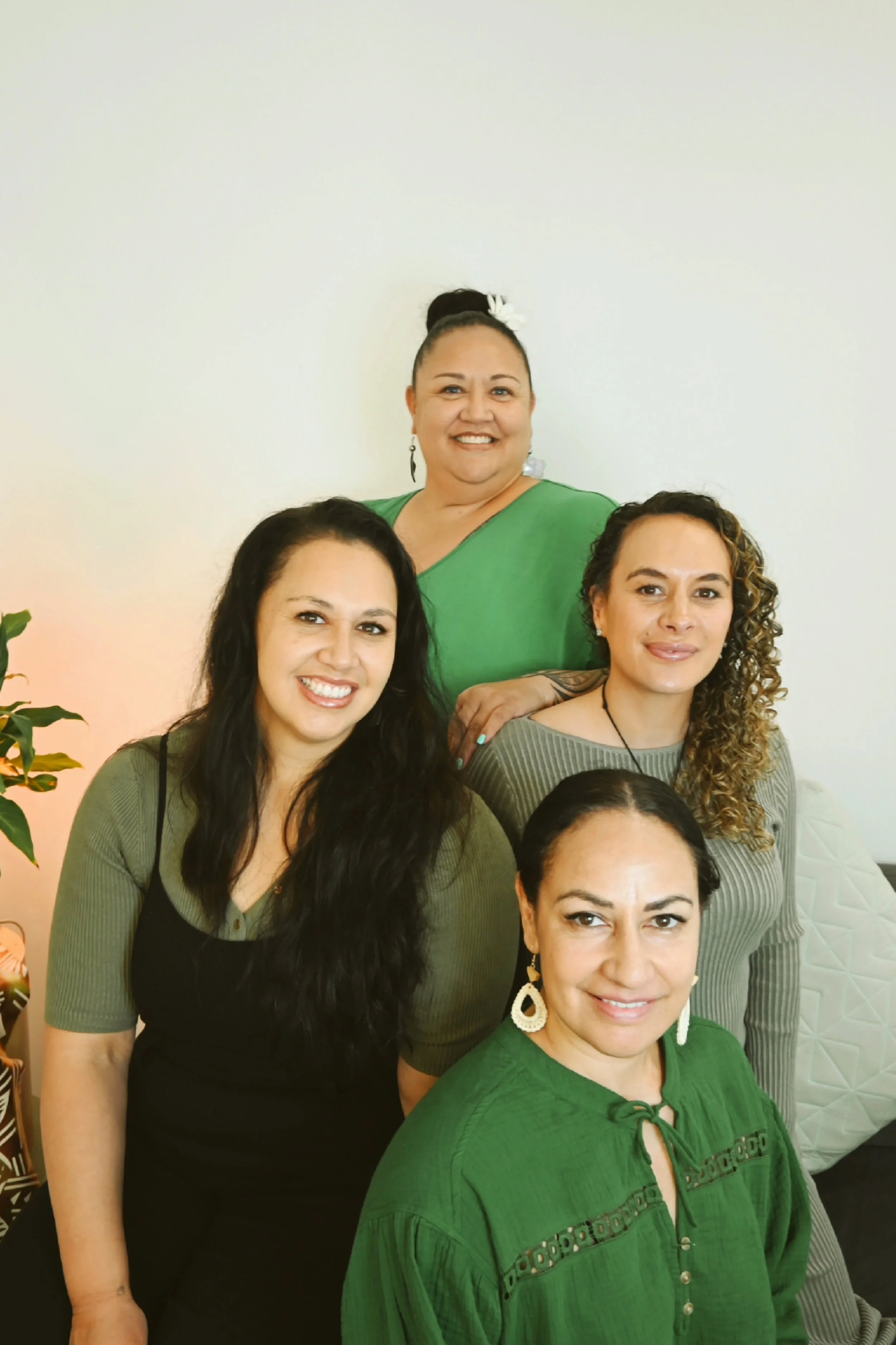 A photo of the four KlovaCare founders wearing tops in different hues of green. Jewellery and background decor showcase their Polynesian heritage.