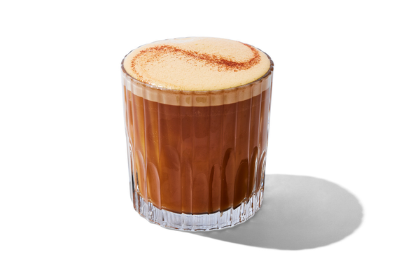 A glass of whipped coffee with a frothy top and sprinkled cinnamon