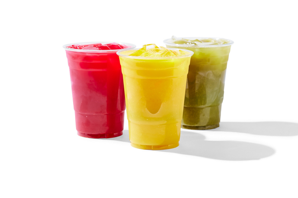 Three cups of colorful frozen beverages, one red, one yellow, and one green, with ice, on a white background.