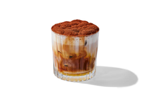 Glass of iced coffee with whipped topping and cocoa powder on top, with ice cubes inside.