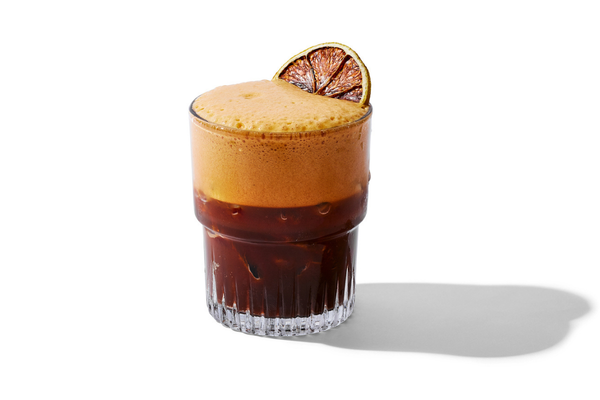 A glass of iced coffee with foam and a lime wedge garnish.