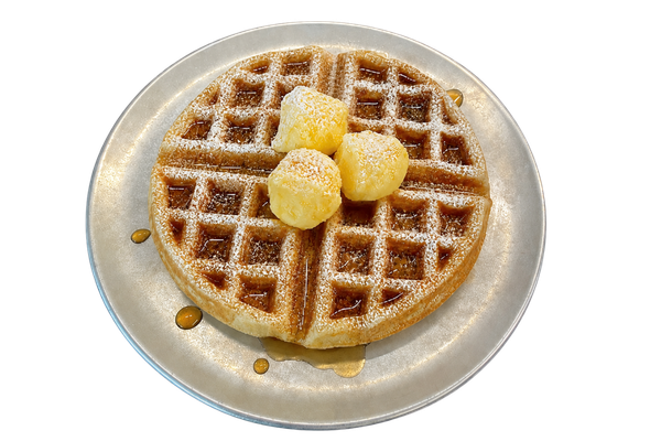 A heart-shaped waffle topped with three scoops of butter, served on a silver plate with syrup drizzled around.