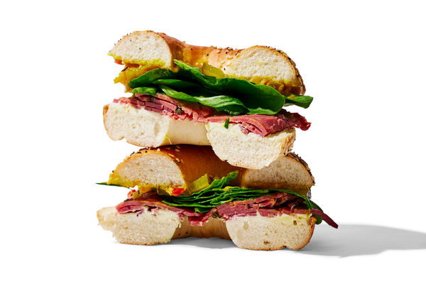 Stacked sandwich with bread, sliced roast beef, and fresh spinach leaves.