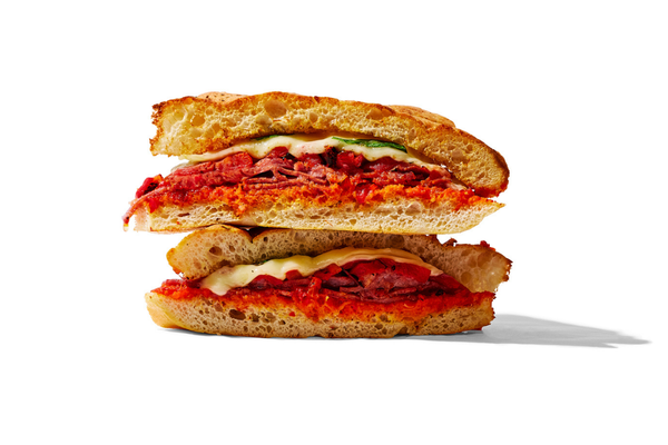 Cross-section of a sandwich with bread, tomato sauce, melted cheese, pepperoni, and vegetables.