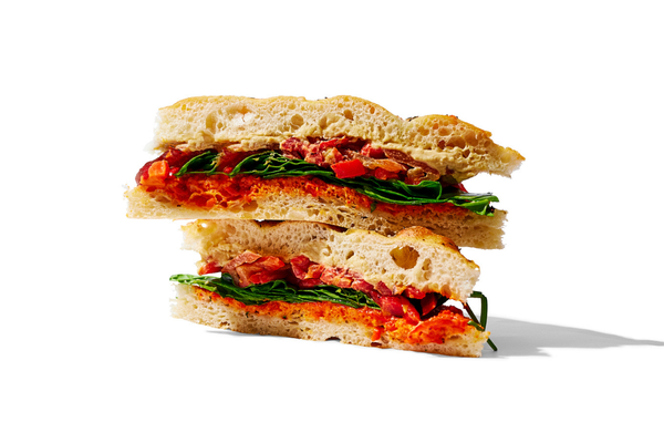 Cross-section of a sandwich with bread, leafy greens, tomato, bacon, and a spread or sauce.