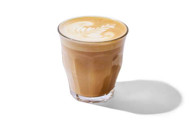 A glass of coffee with latte art on top, placed on a white background.