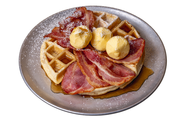 Waffles topped with three scoops of butter, crispy bacon, powdered sugar, and syrup on a plate.