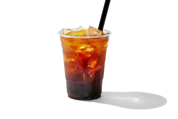 A transparent plastic cup filled with iced coffee or soda and ice cubes, with a black straw, casting a shadow on a white background.
