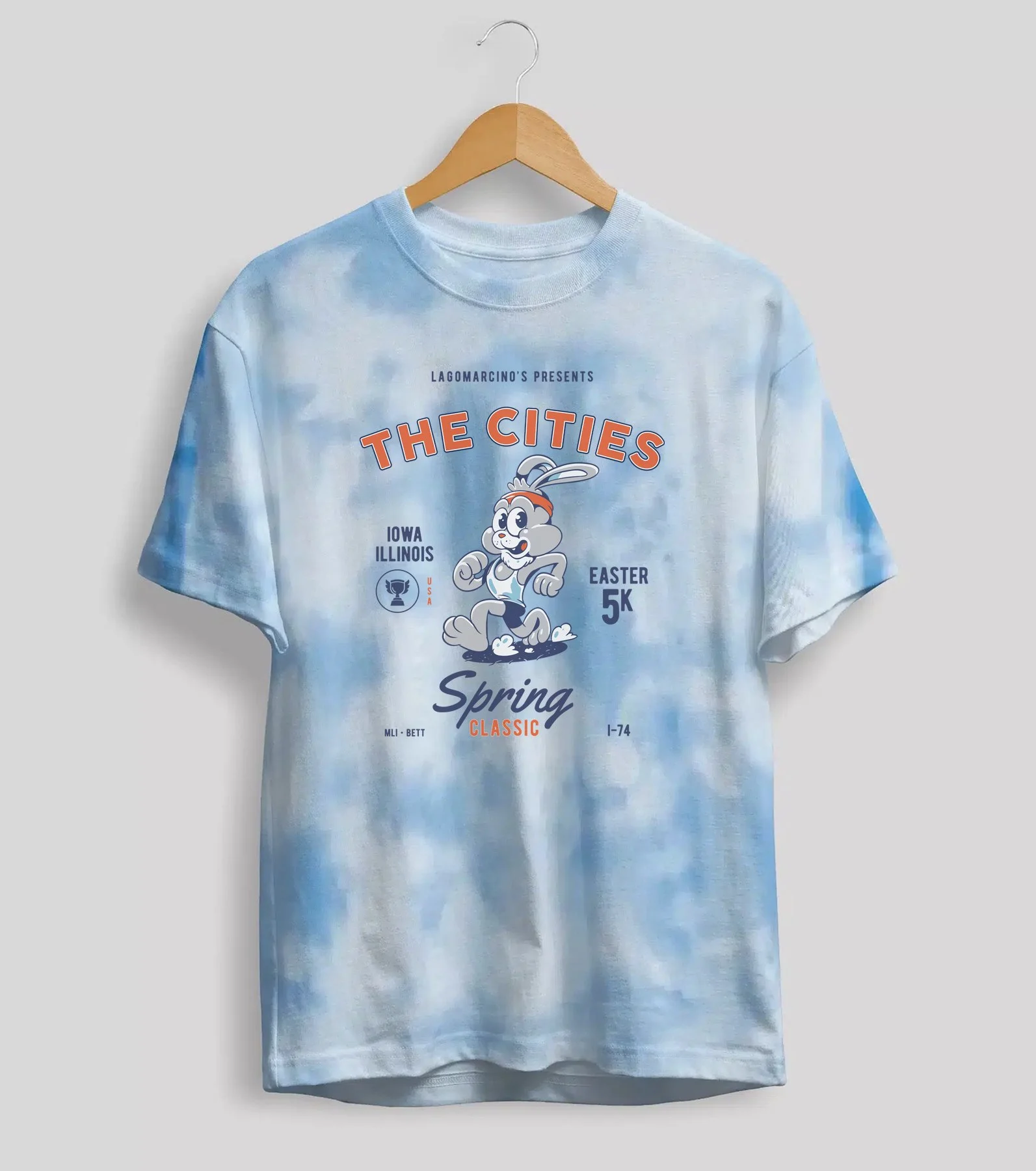 Light blue tie-dye T-shirt hanging on a wooden hanger with graphic text and cartoon bunny mascot for a spring race event.
