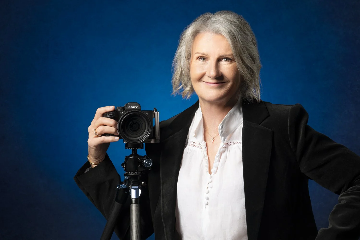 Diane Armstrong with her camera on a tripod against a deep blue backdrop