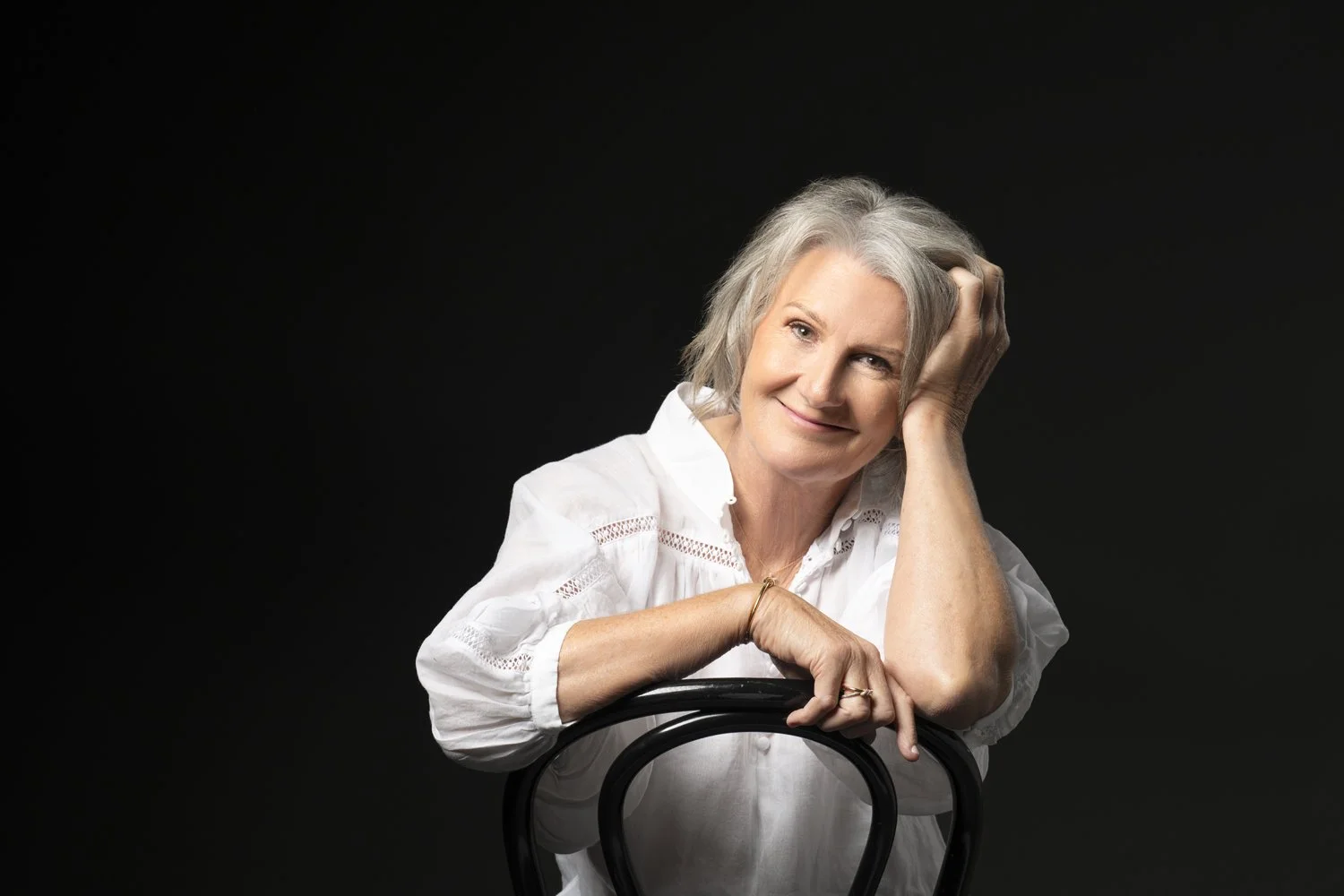 Diane Armstrong leaning on the back of a chair, dressed in black