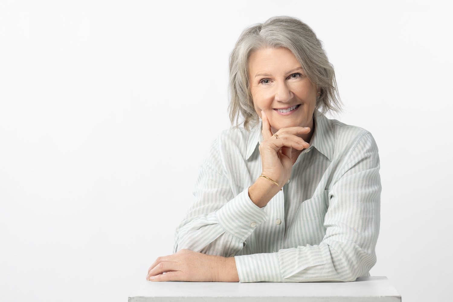 Diane Armstrong resting her chin on her hand, smiling, against a white backdrop