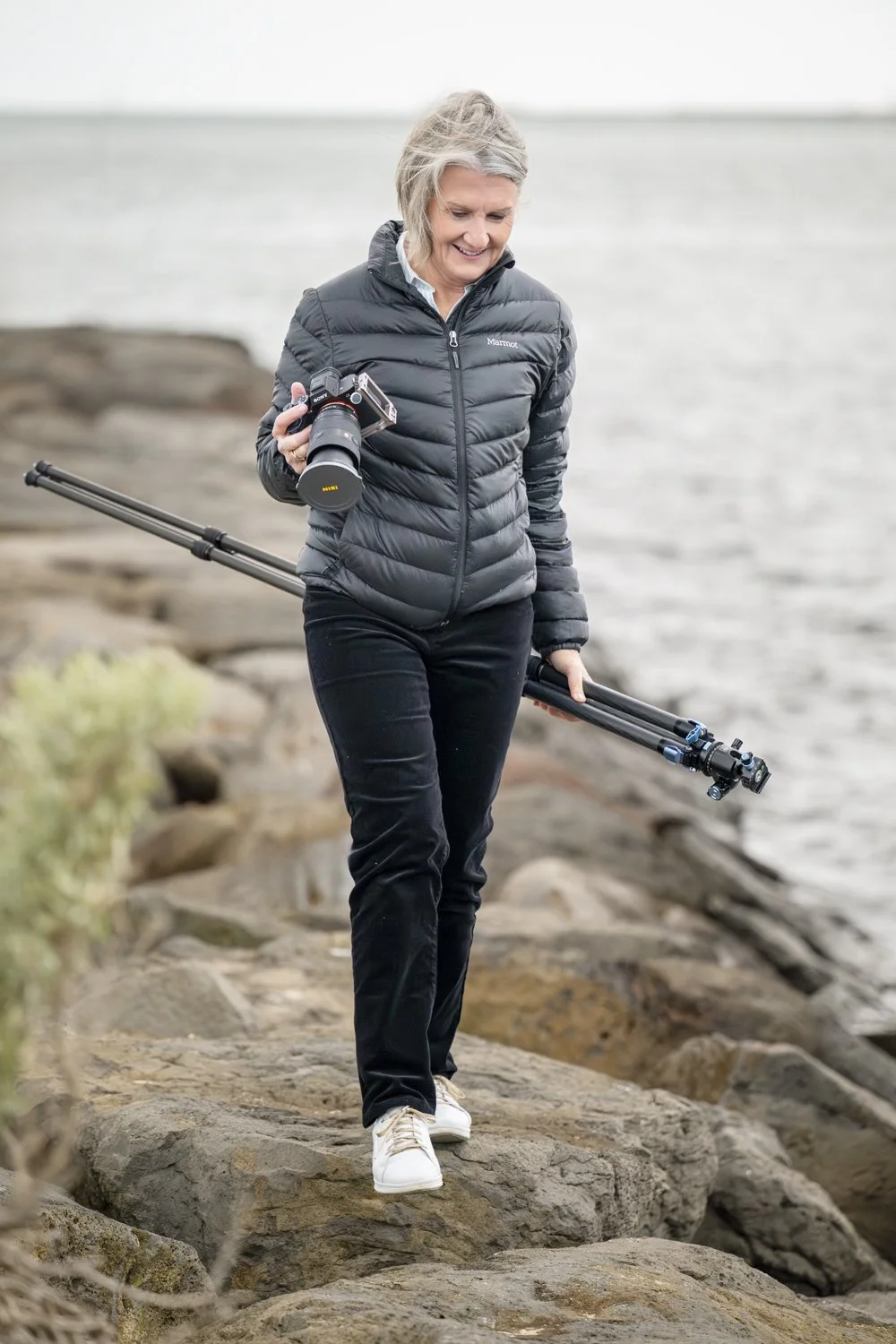 Diane Armstrong with her camera and tripod among coastal rocks