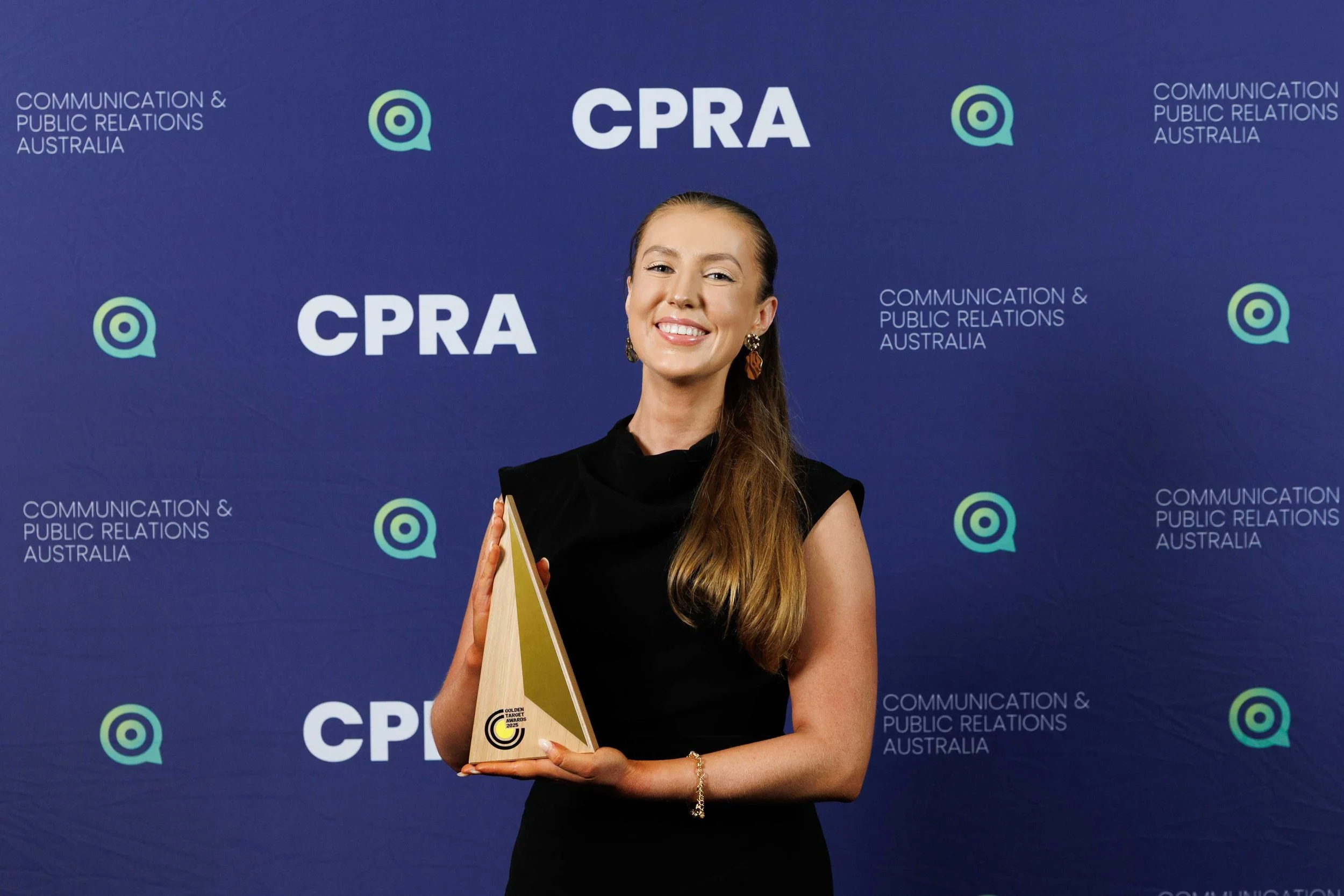 An image of Gold Emerging Leader of the Year - Agency Award recipient Tayla Harvey from We Are Brooklyn in front of the Communication and Public Relations Australia photo wall.