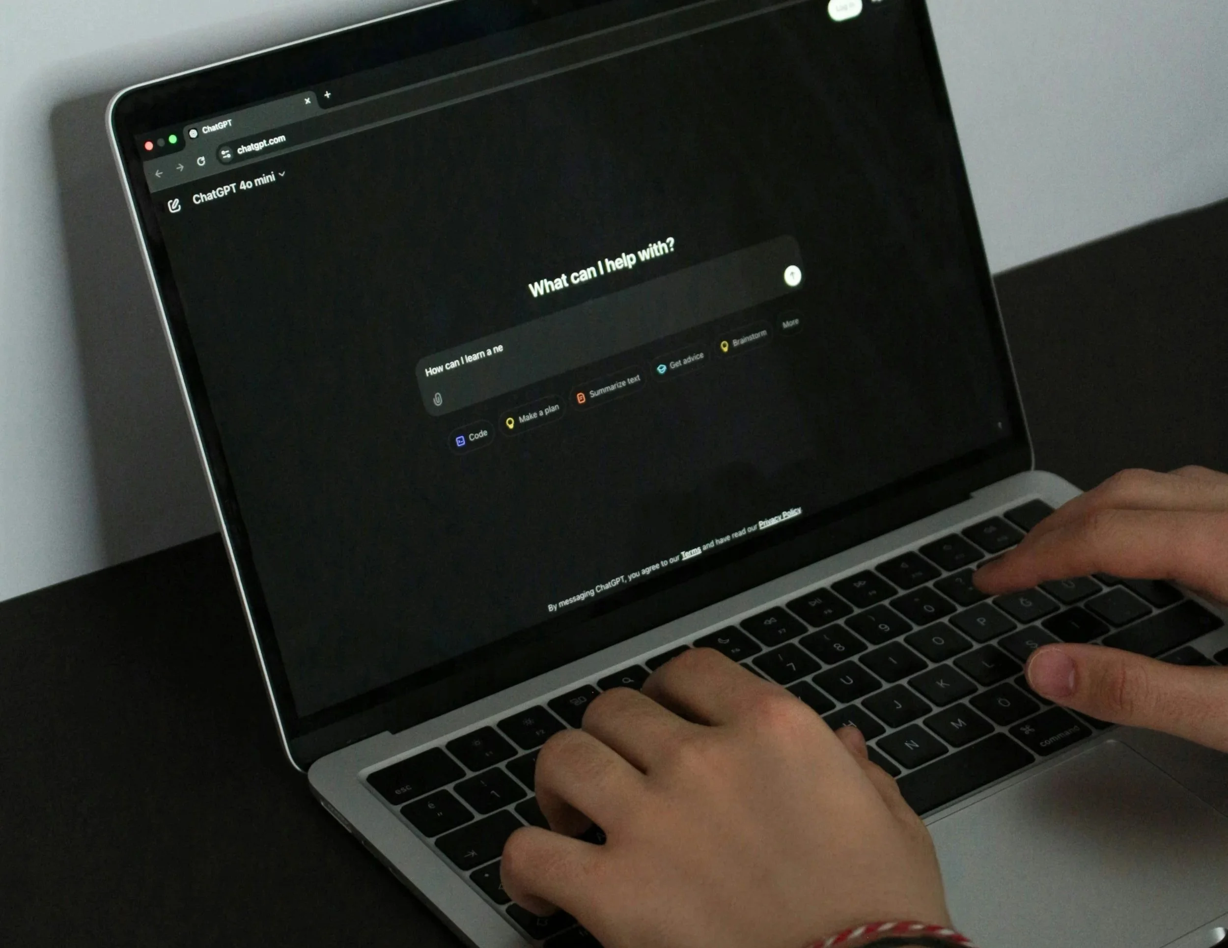 A close-up of a laptop on the page of ChatGPT, hands typing prompt.